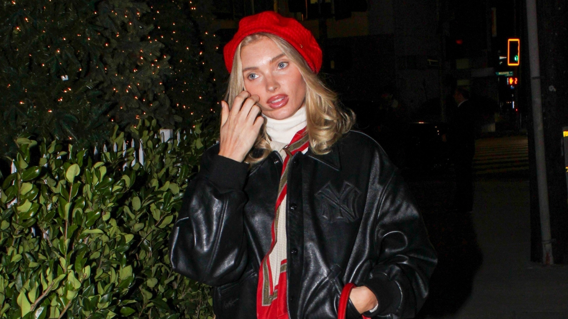 Elsa Hosk wearing a red beret, cream turtleneck, silk scarf, black leather bomber jacket, cream trousers, and black leather loafers to a Ralph Lauren event in Los Angeles