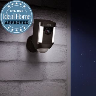 A ring security camera with a movement sensor and security light on a brick wall at night with the Ideal Home approved logo