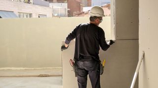 Man on building site in hard hat cutting plasterboard to fit walls 