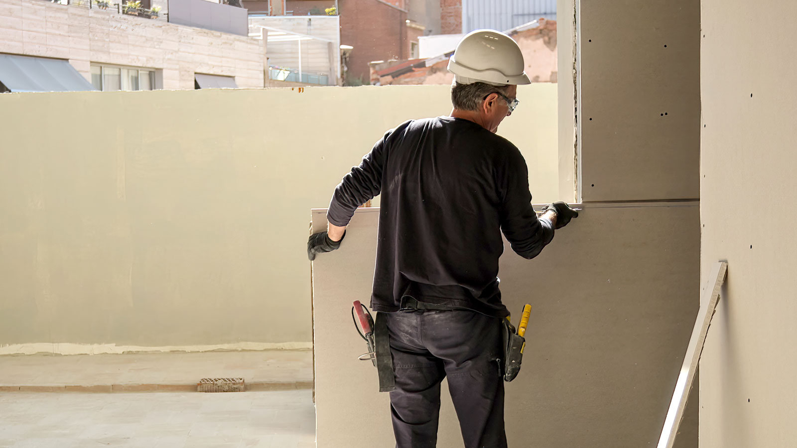 Man on building site in hard hat cutting plasterboard to fit walls 