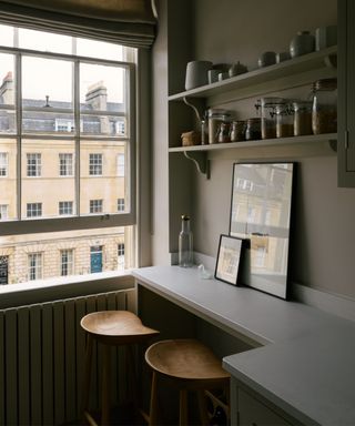 A recessed kitchen counter has been used to create a small breakfast nook with two bar stools next to a large sash window