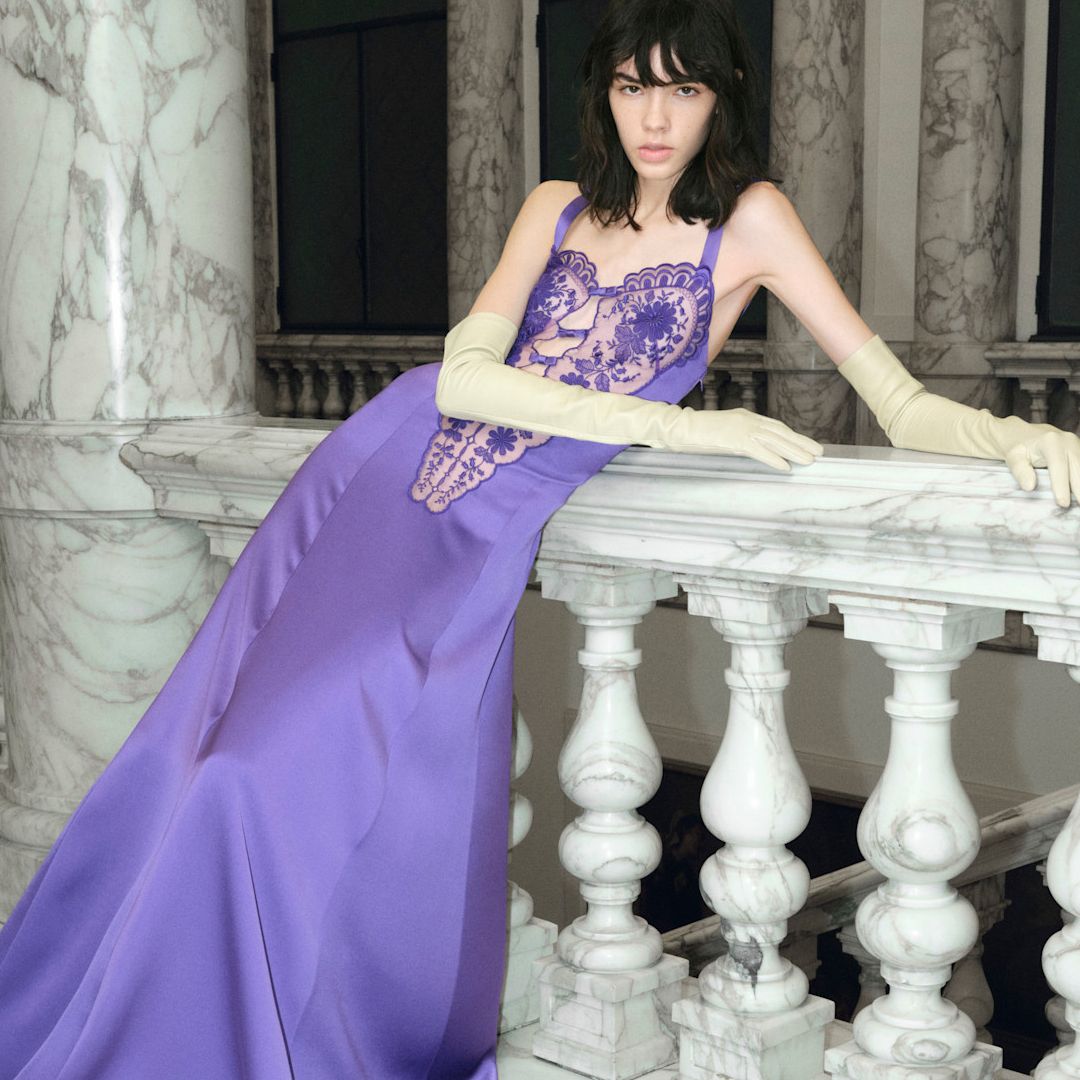 A model wearing a purple gown. She is surrounded by bottles of iris perfumes. 