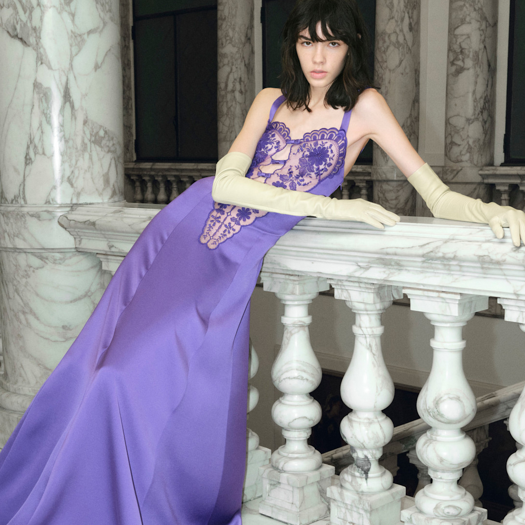 A model wearing a purple gown. She is surrounded by bottles of iris perfumes. 