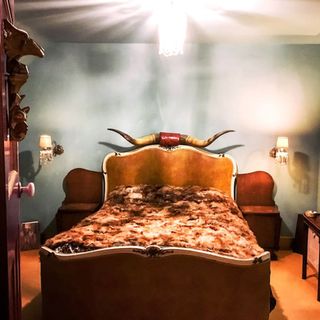 bedroom with blue wall brown bed with bison horn headboard wall lamps and brown floor