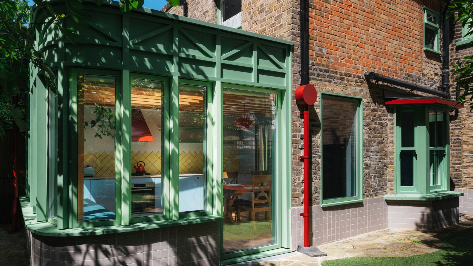 Exterior of the back of the house with green window trims and red pipe details