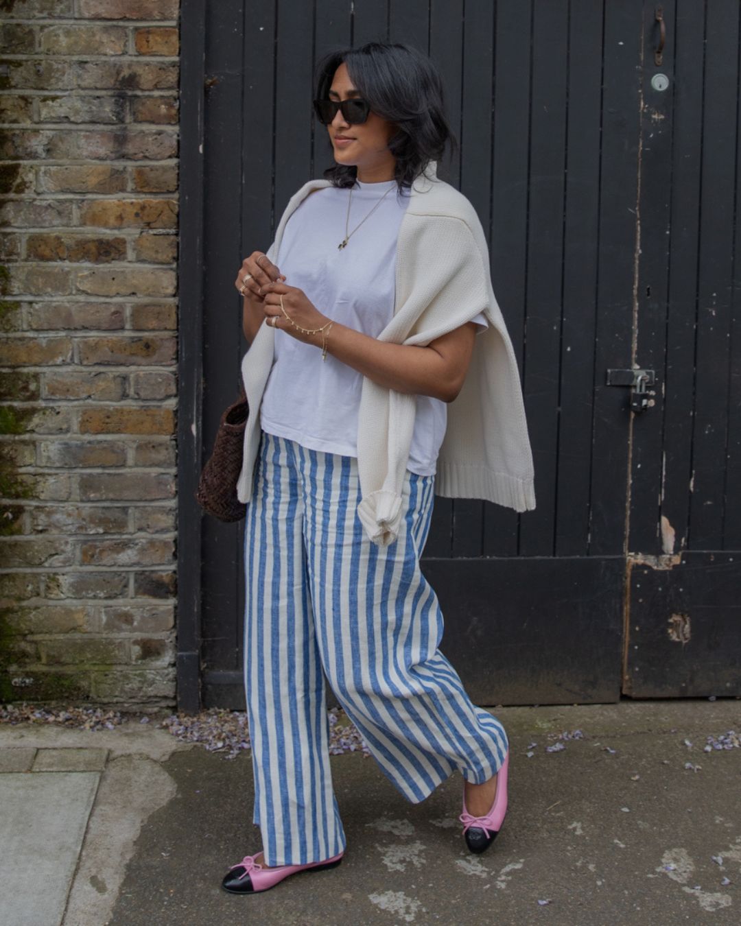 @chiarasatelier wears Boden's blue and white stripe linen trousers, a white t-shirt, cream jumper, pink Chanel ballet flats and black sunglasses