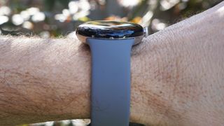En Google Pixel Watch med ett blått armband visas upp runt en handled sett från sidan.