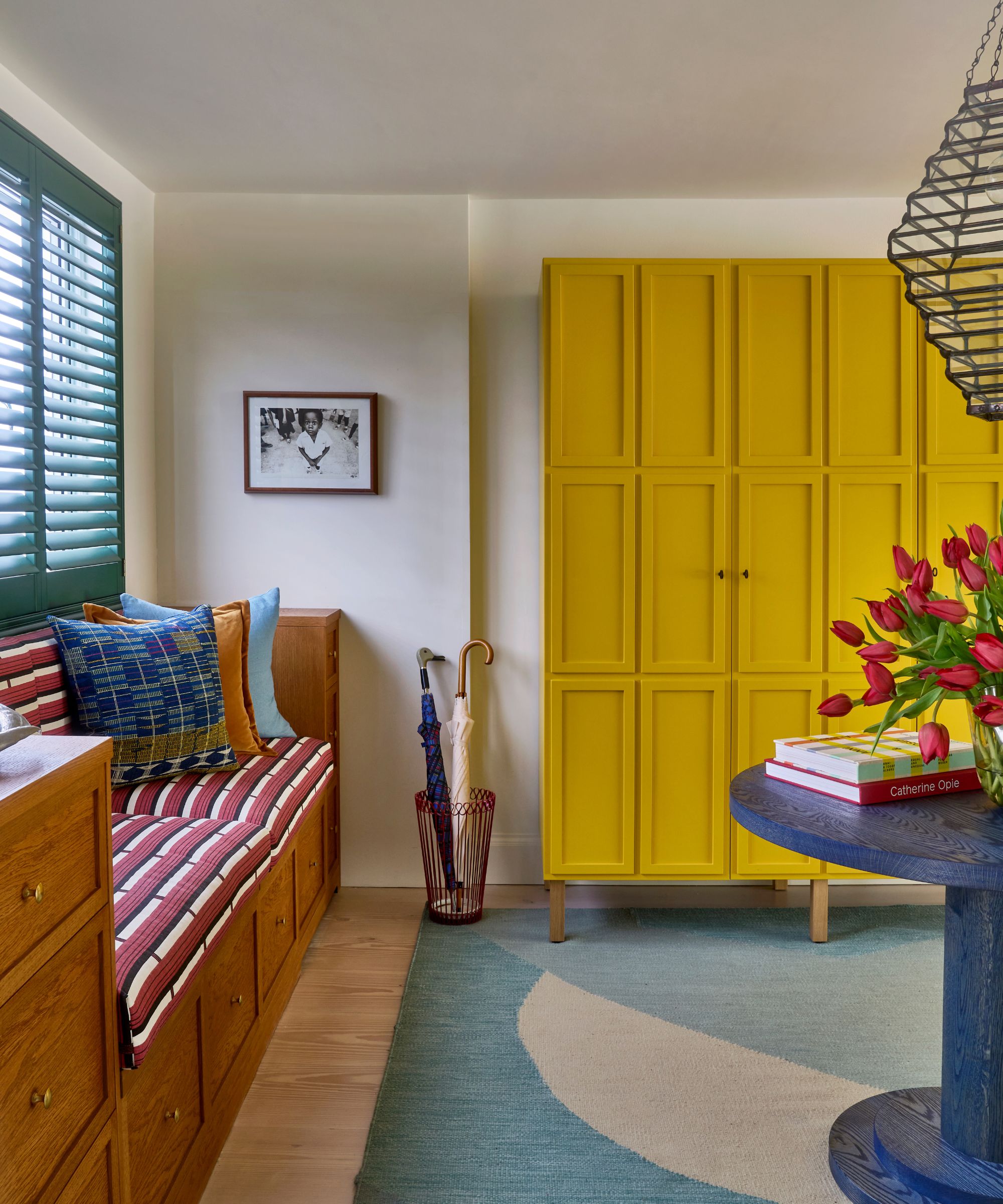 Entryway with blue abstract rug, large blue round table, built-in wooden bench with geometric cushions, and large yellow painted storage unit