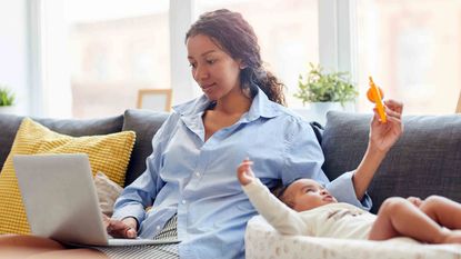 A mother waves a toy in front of her baby while working on the computer.