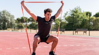 a man squatting with a resistance band under his feet and stretching above his head with his hands