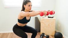 Woman squats as she lifts two dumbbells in front of her