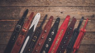 Assorted guitar straps lie on a wooden floor