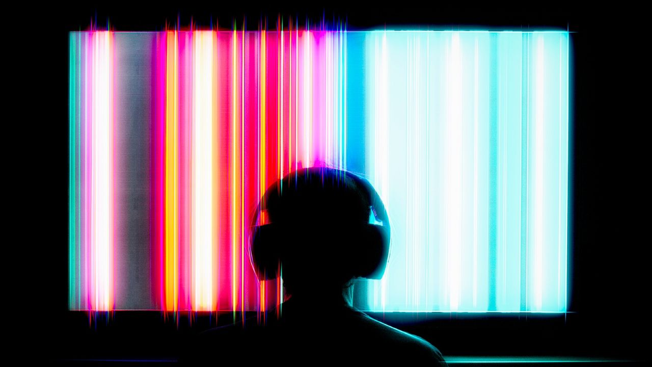 A person with headphones on sits in front of a multicolor TV screen