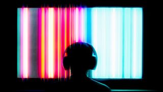 A person with headphones on sits in front of a multicolor TV screen