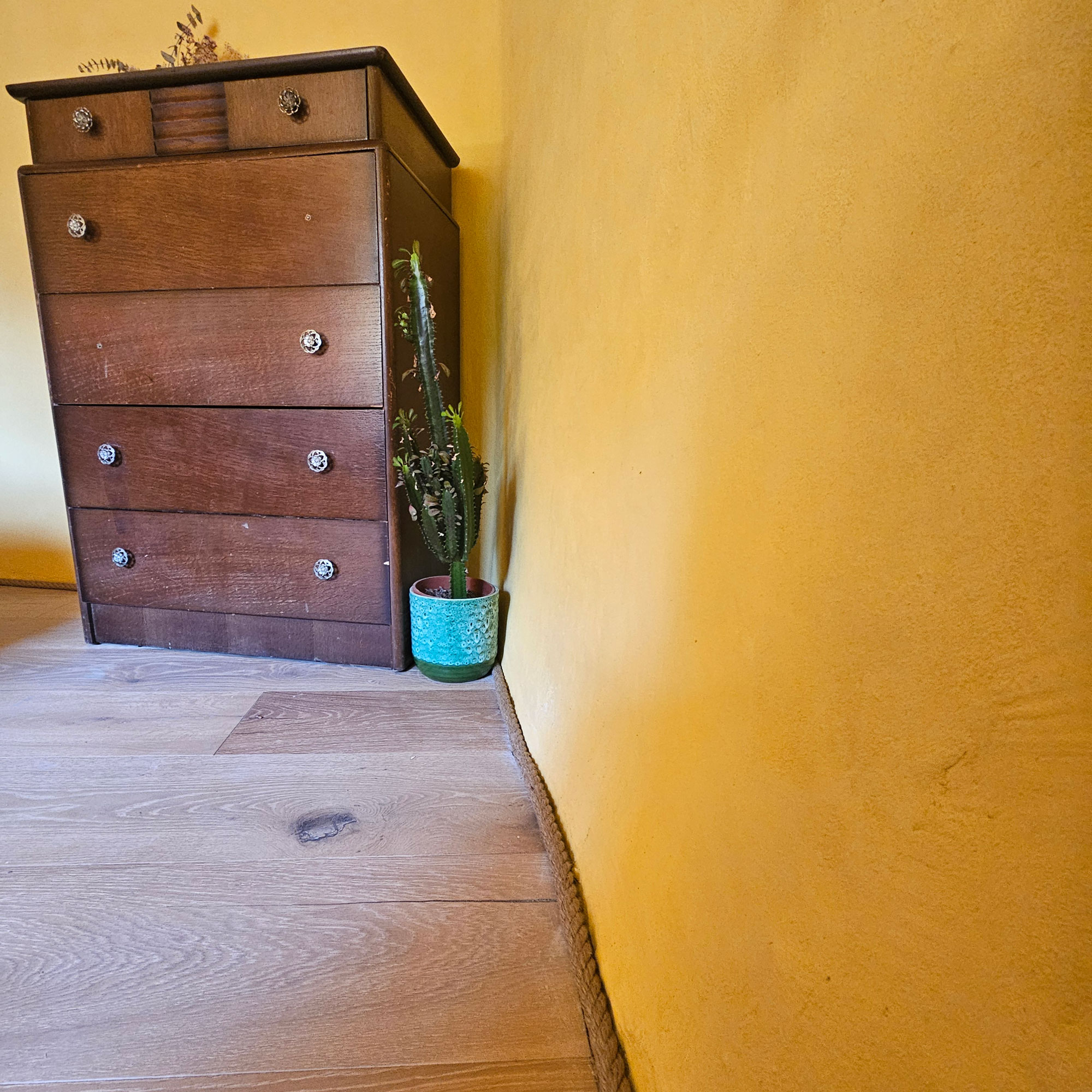 Yellow limewashed room with rope skirting board and brown wood furniture