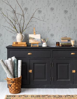Green gray wallpapered walls in hallway with black chest and trinkets