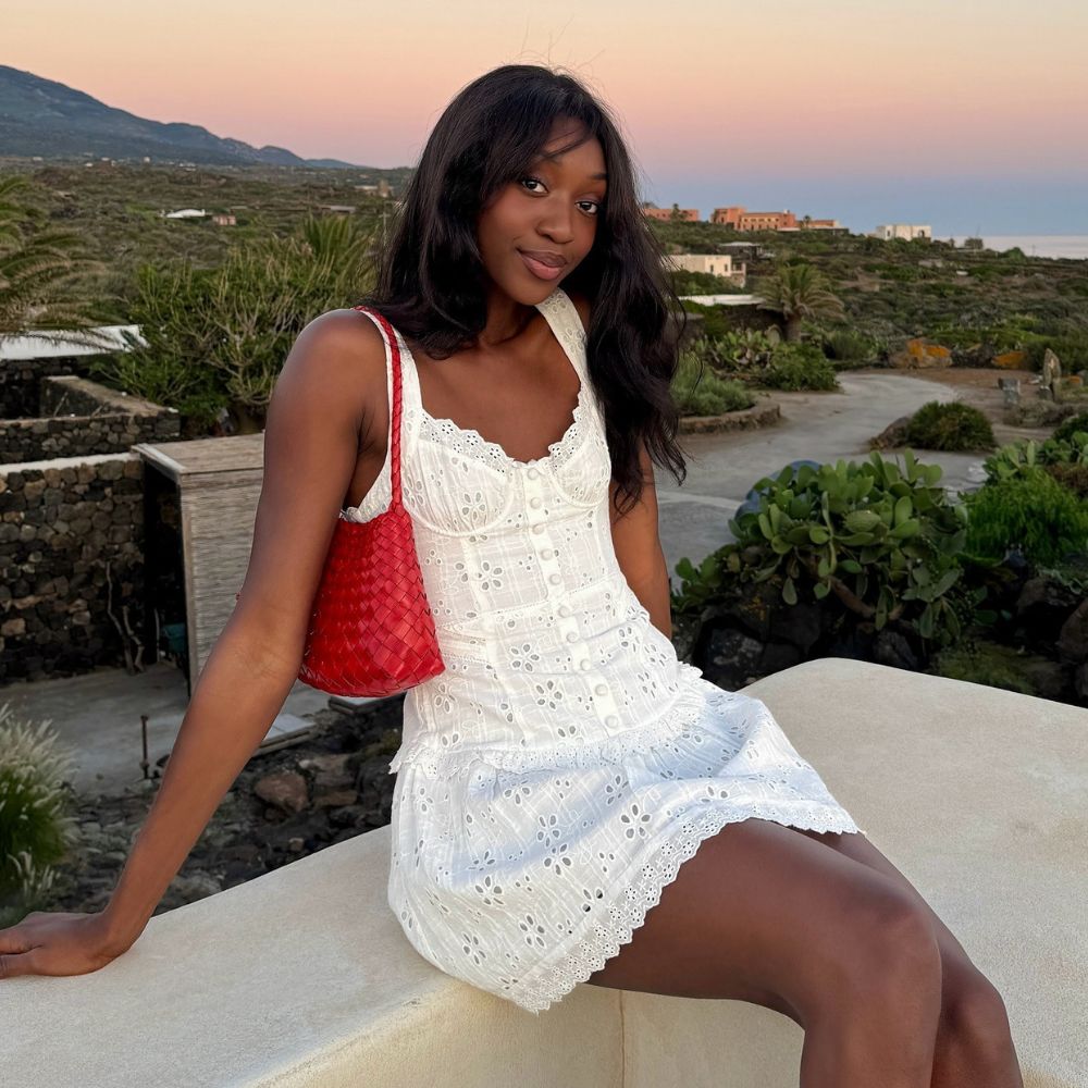 Influencer @emmanuellek_ wears a white mini broderie dress with a red woven shoulder bag.