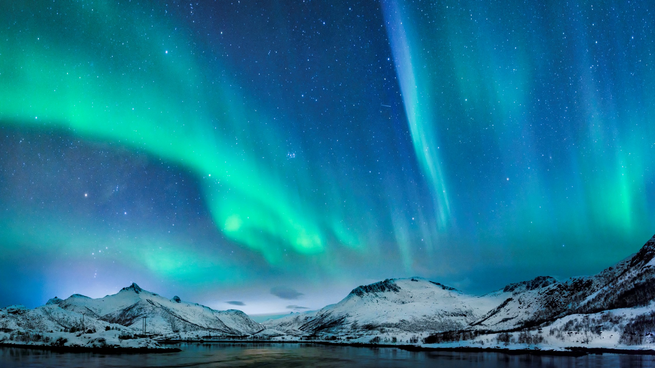 Aurora borealis, ribbons of green and blue streak across the sky above snow-capped hills.