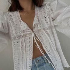 Influencer wears a white tie-front blouse with embroidery partially unbuttoned and styled with jeans.