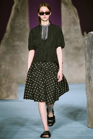 Model wears a black satin top with puffed sleeves with a black and white polka dot skirt