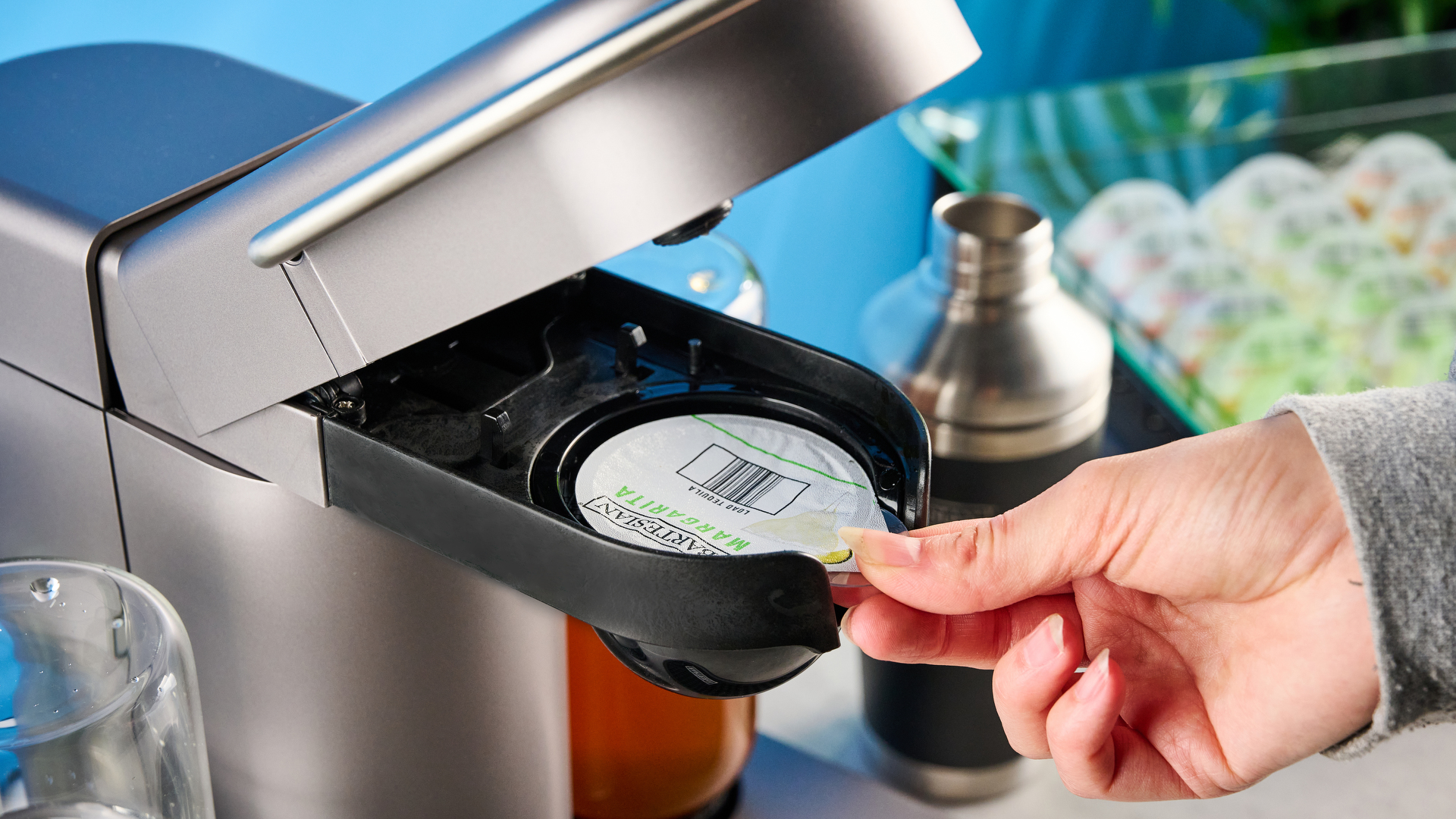 the bartesian premium cocktail machine photographed against a blue background showing its drink-making abilities and accessories and functionality with cocktail pods