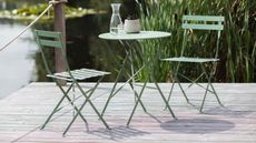 A green metal bistro set on decking overlooking a lake