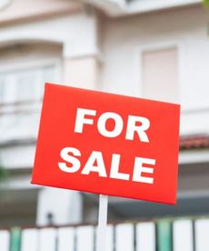 Blurred exterior of home with red For Sale sign in center and focus