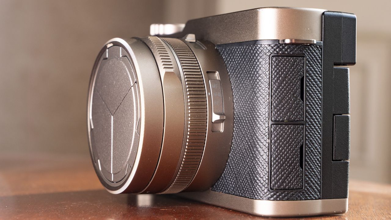 Side on of the Titanium Gold special edition of the Panasonic Lumix L10 compact camera, on an antique wooden table