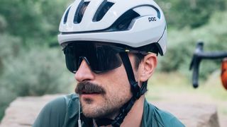 A white man with a moustache wears a pair of 100% Hypercraft cycling glasses