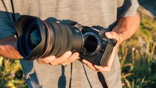 A photographer mounting a Canon RF 15-35mm f/2.8 lens to a Canon EOS R6 Mark II camera, outdoors in the fading sun