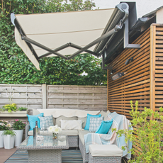 A cream awning over grey garden furniture with turquoise cushions.