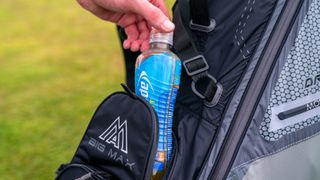 A golfer putting a bottle of juice in a golf bag