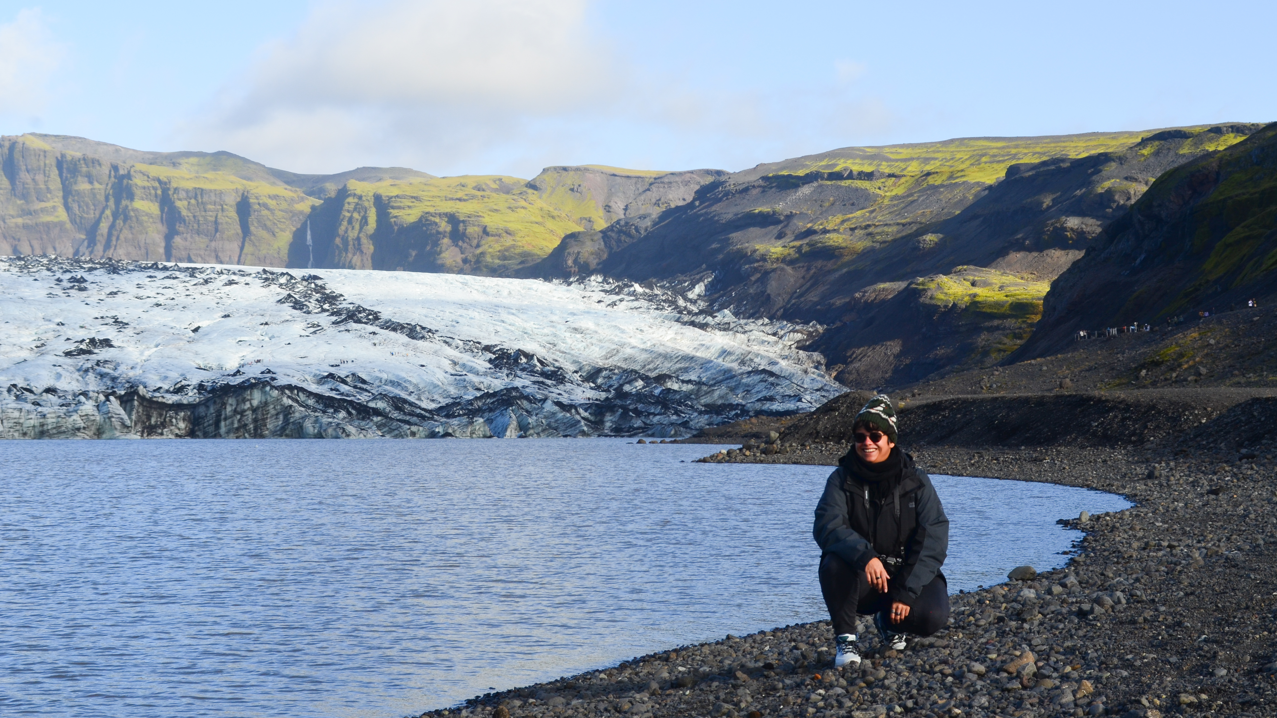 A person crouching in front of a glacier