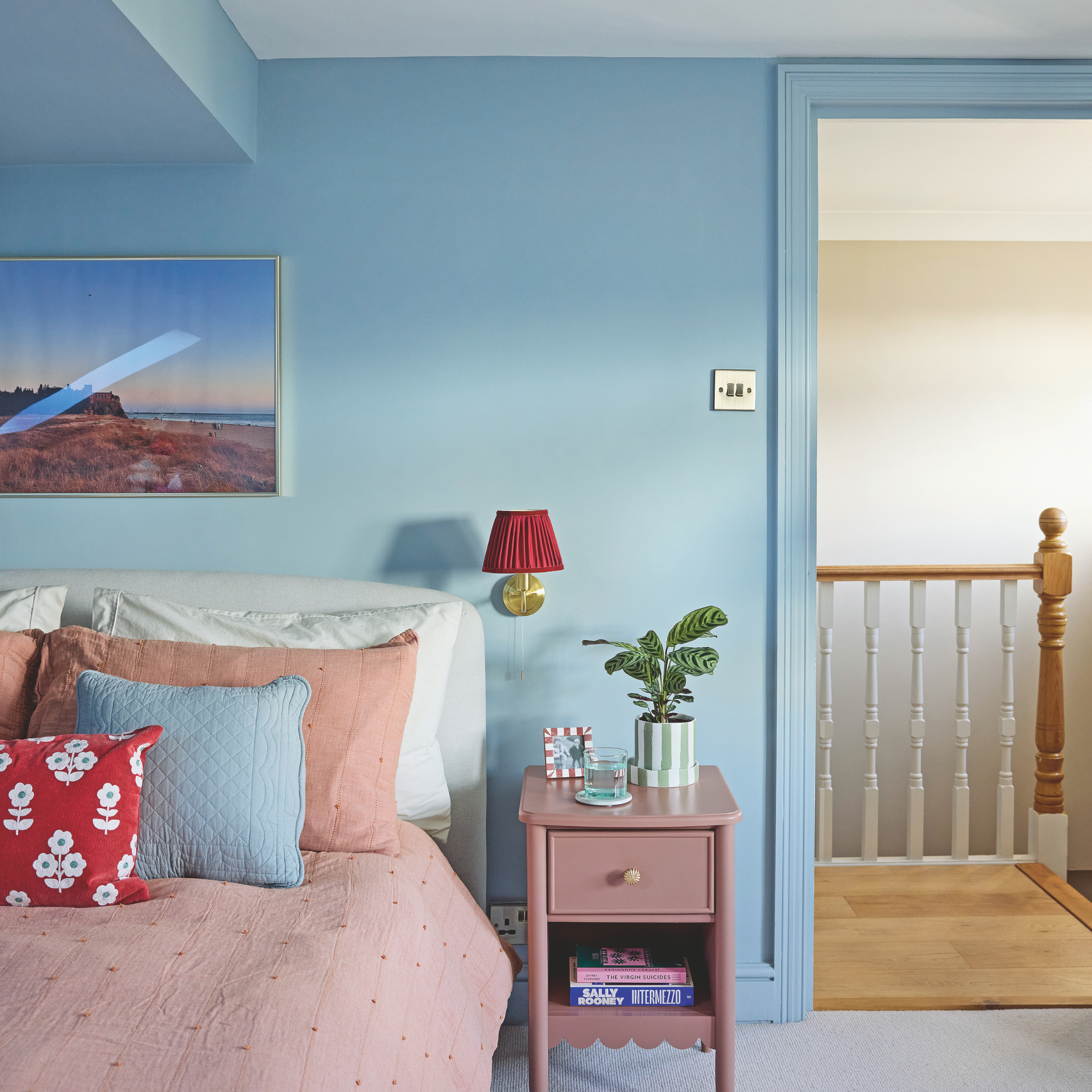 Pale blue painted bedroom with pink bedside table and pink bedding.