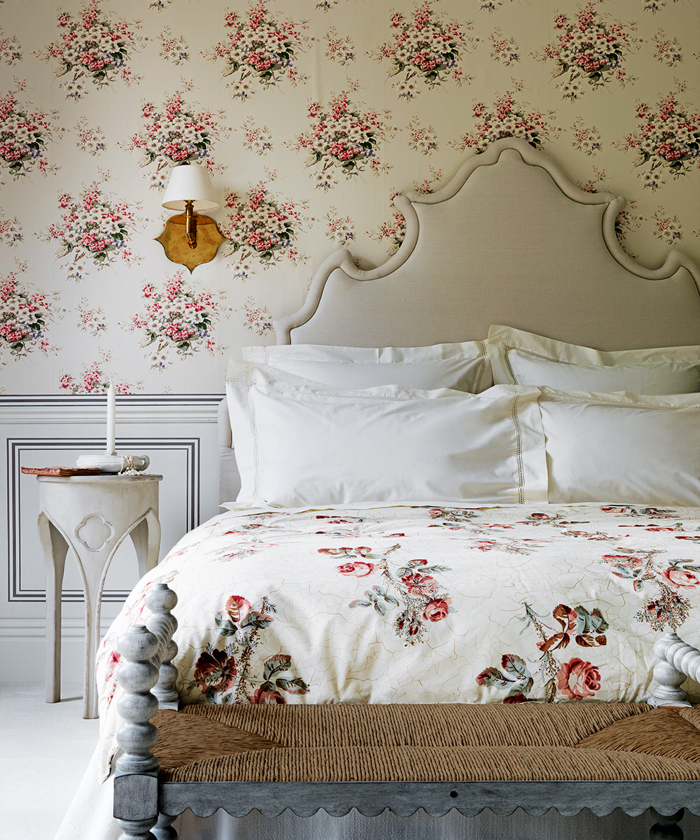 An example of traditional bedroom wallpaper ideas in a floral print, with a statement headboard and floral bedlinen in front.