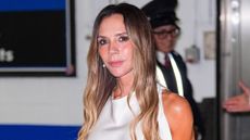 Image of Victoria Beckham smiling with curled long brunette hair with bright blonde ombre highlights and wearing a white dress