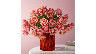30 pink tulips inside a red glass vase sitting on a table, for the best flower delivery services.
