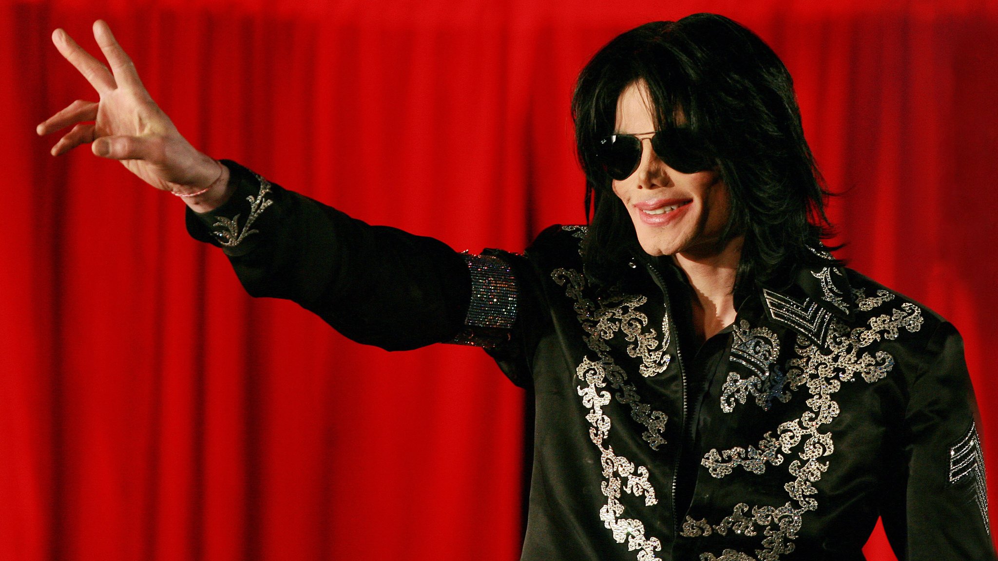 Michael Jackson waves in black sunglasses against a red curtain as fans prepare to watch Michael Jackson: The Trial online from Feb 4, 2026