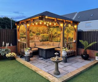 A wooden garden gazebo over a paved patio area with a patterned shower curtain design as a backdrop