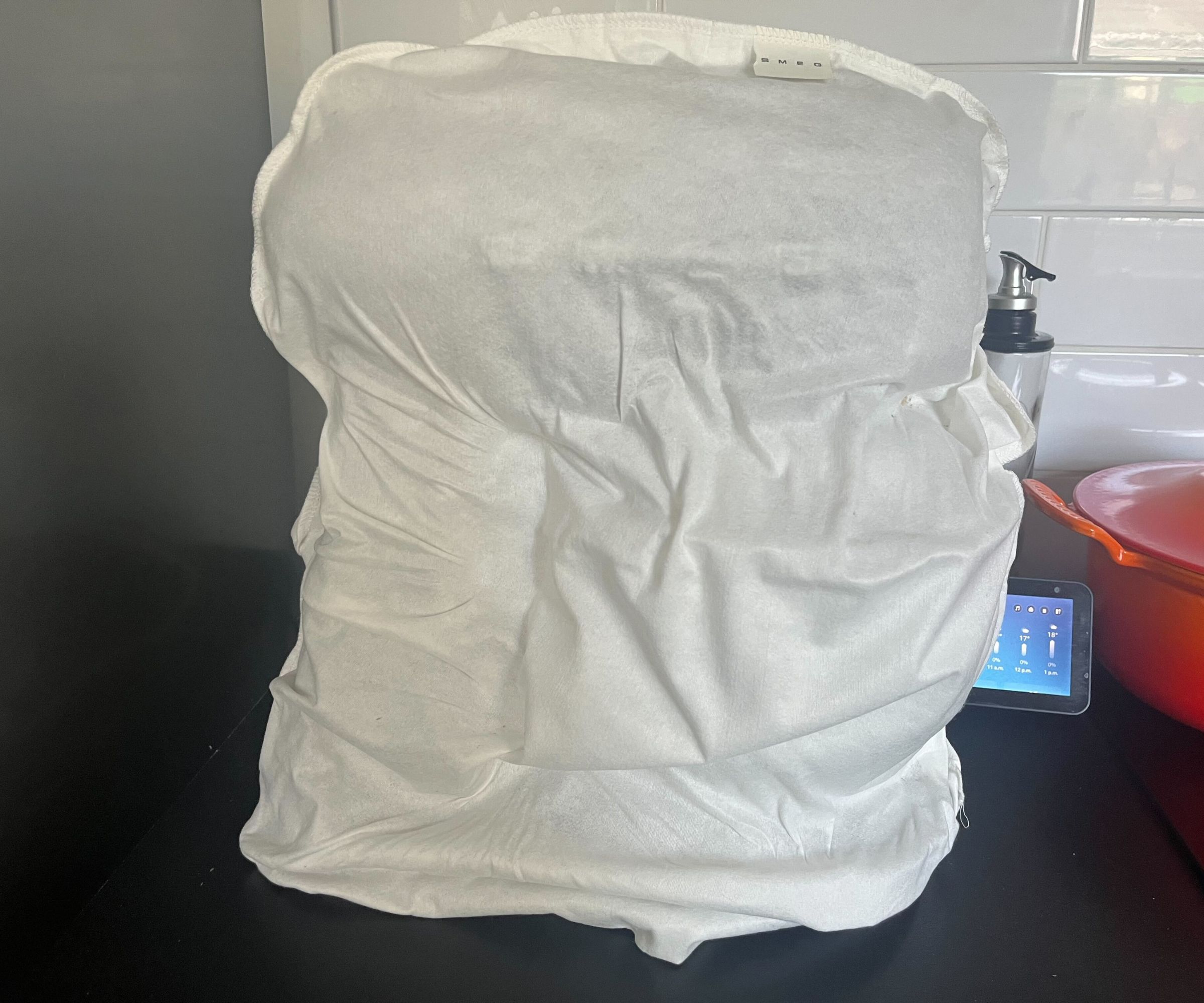 A stand mixer covered with a white cotton bag on a counter. 