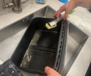 Cleaning the Ninja Foodi FlexBasket Air Fryer in a sink with soapy water.