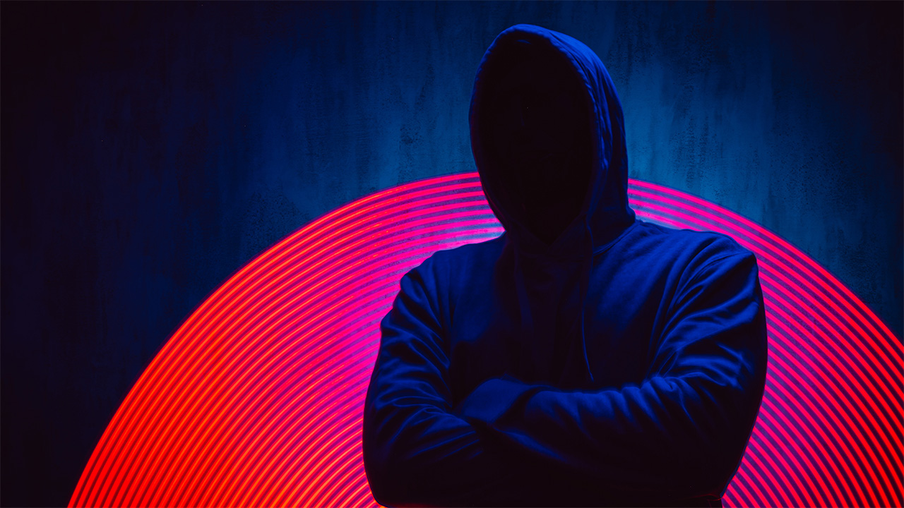 Shadowy hooded figure stood crossed armed in front of red and dark blue background