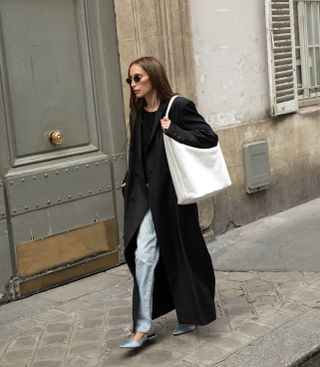 Chloe Harrouche wearing a black coat, jeans, and a light blue pair of Loulou Studio shoes.