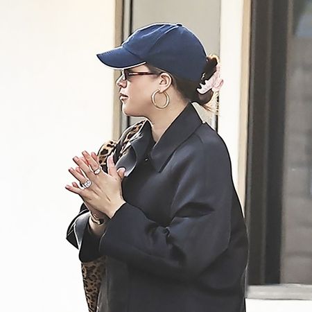 Sofia Richie wearing a black coat, navy baseball hat, black pants, red flats, and a leopard print shoulder bag