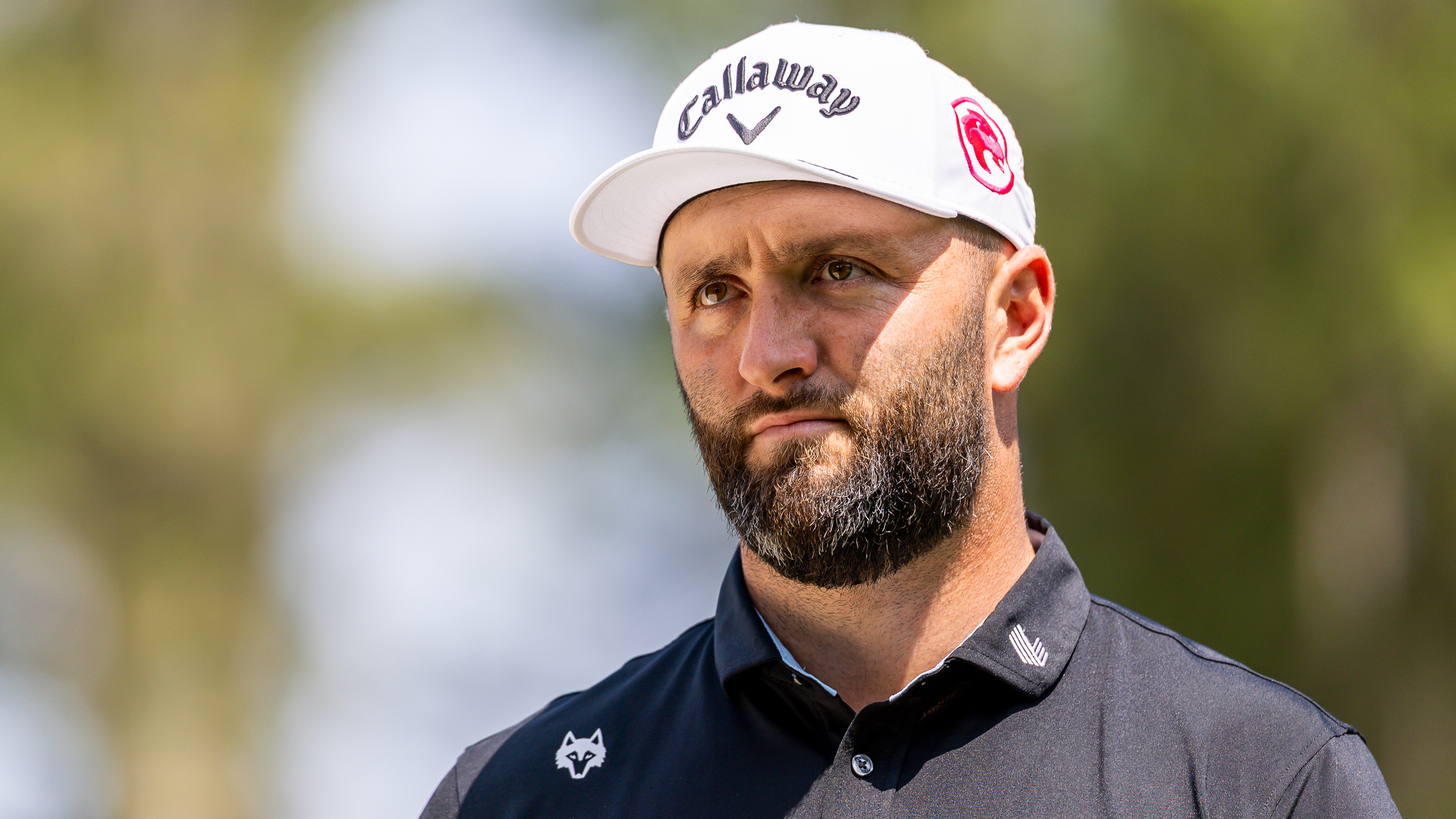 Jon Rahm from the shoulders up wearing a black polo and white Callaway cap