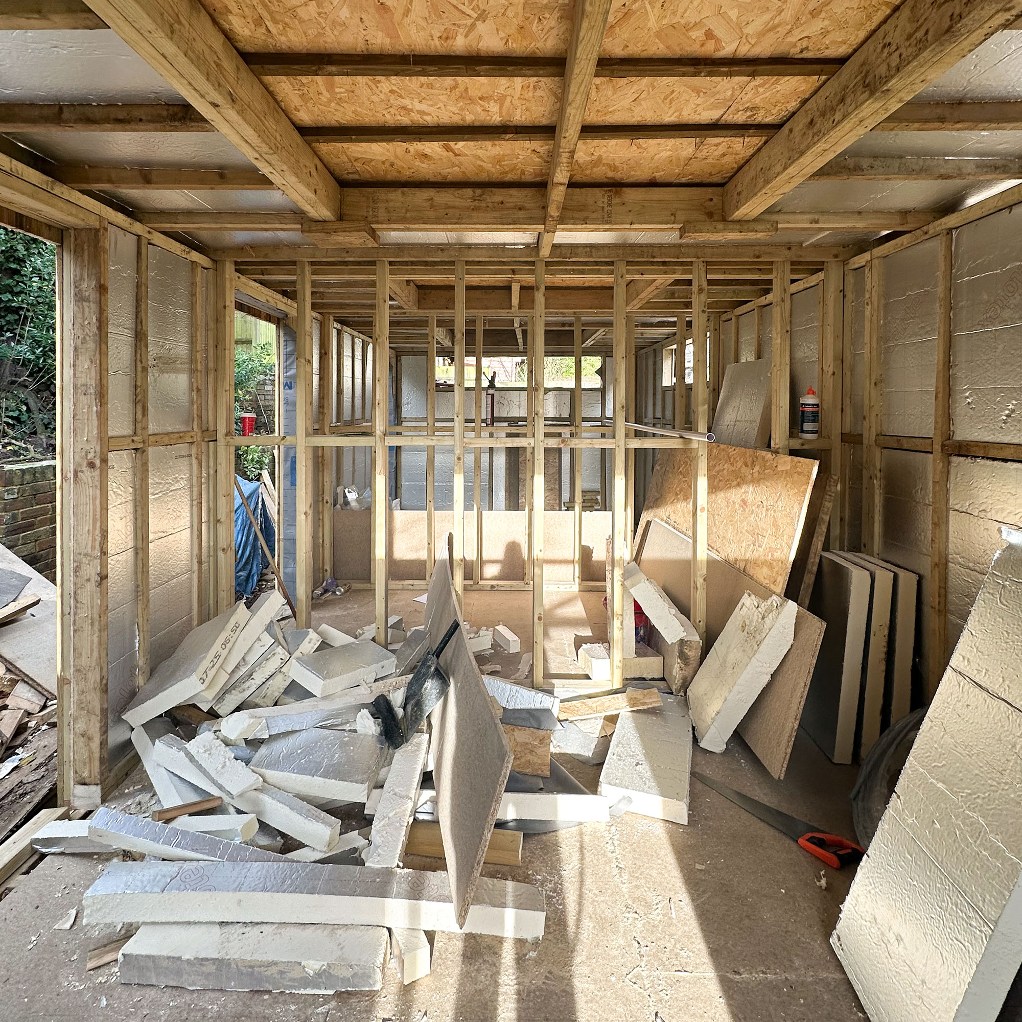 Interior of building while being built, with beams and wall joints all exposed, and building materials on floor