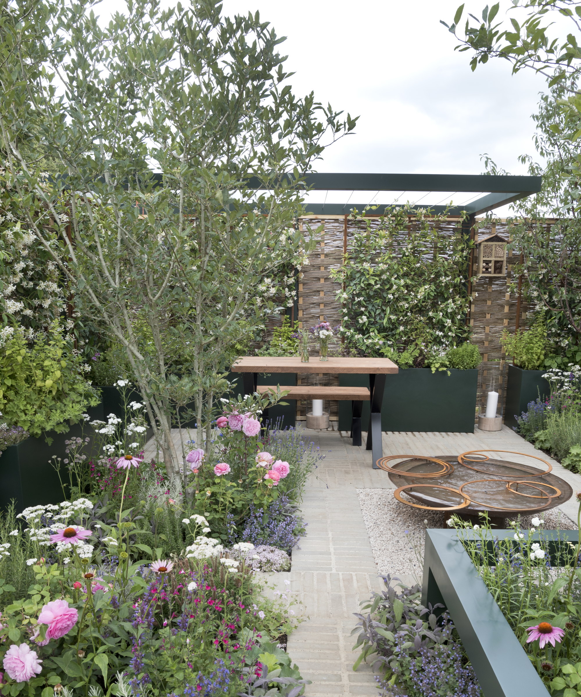 Trees and perennials planted in beds into a stone patio at the Hampton Court Flower Show