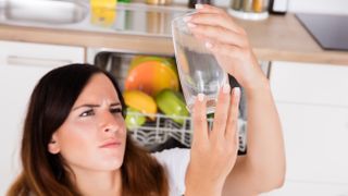A woman looking at a glass closely in front of a dishwasher