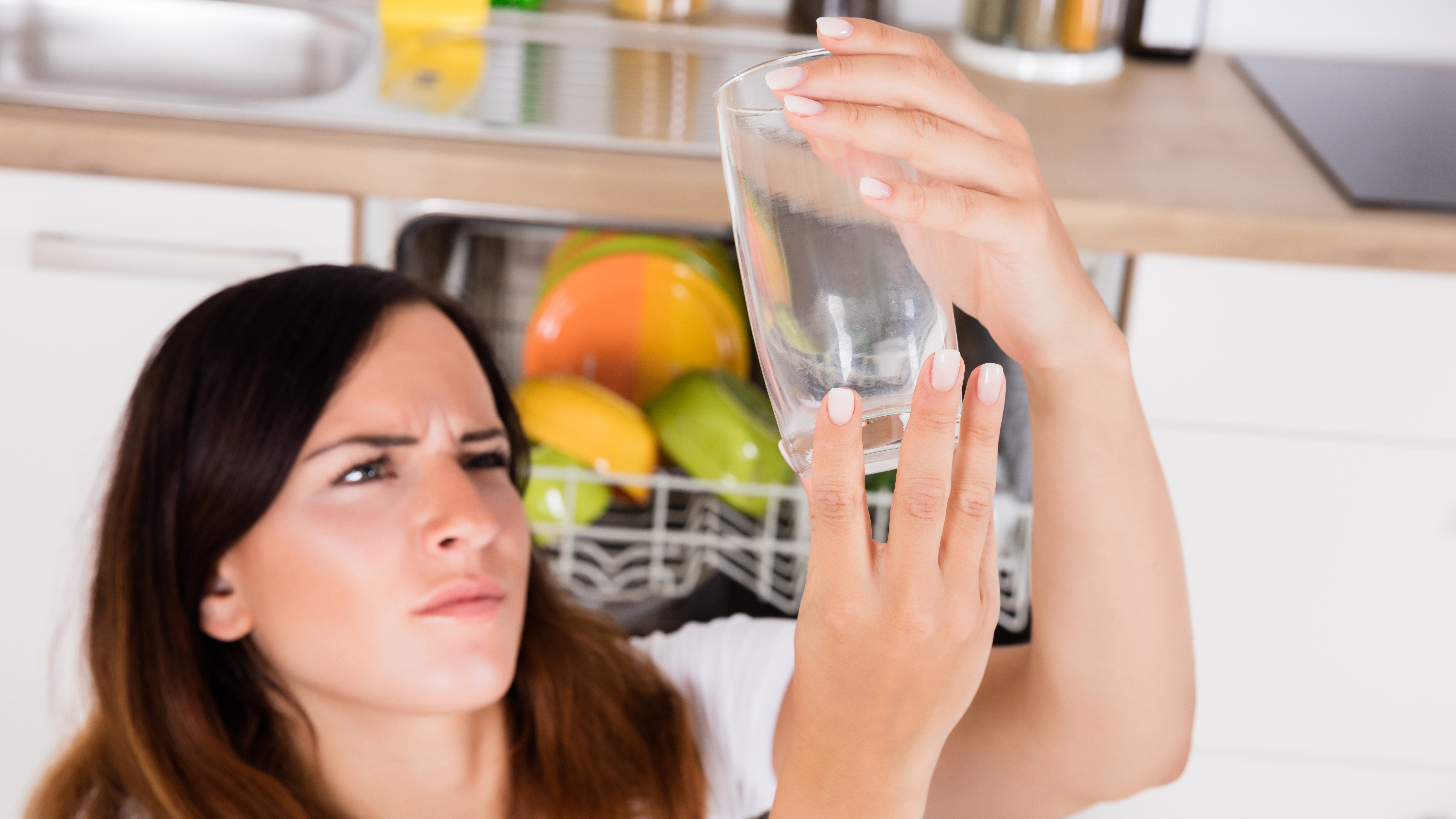 Женщина внимательно смотрит на стакан перед посудомоечной машиной