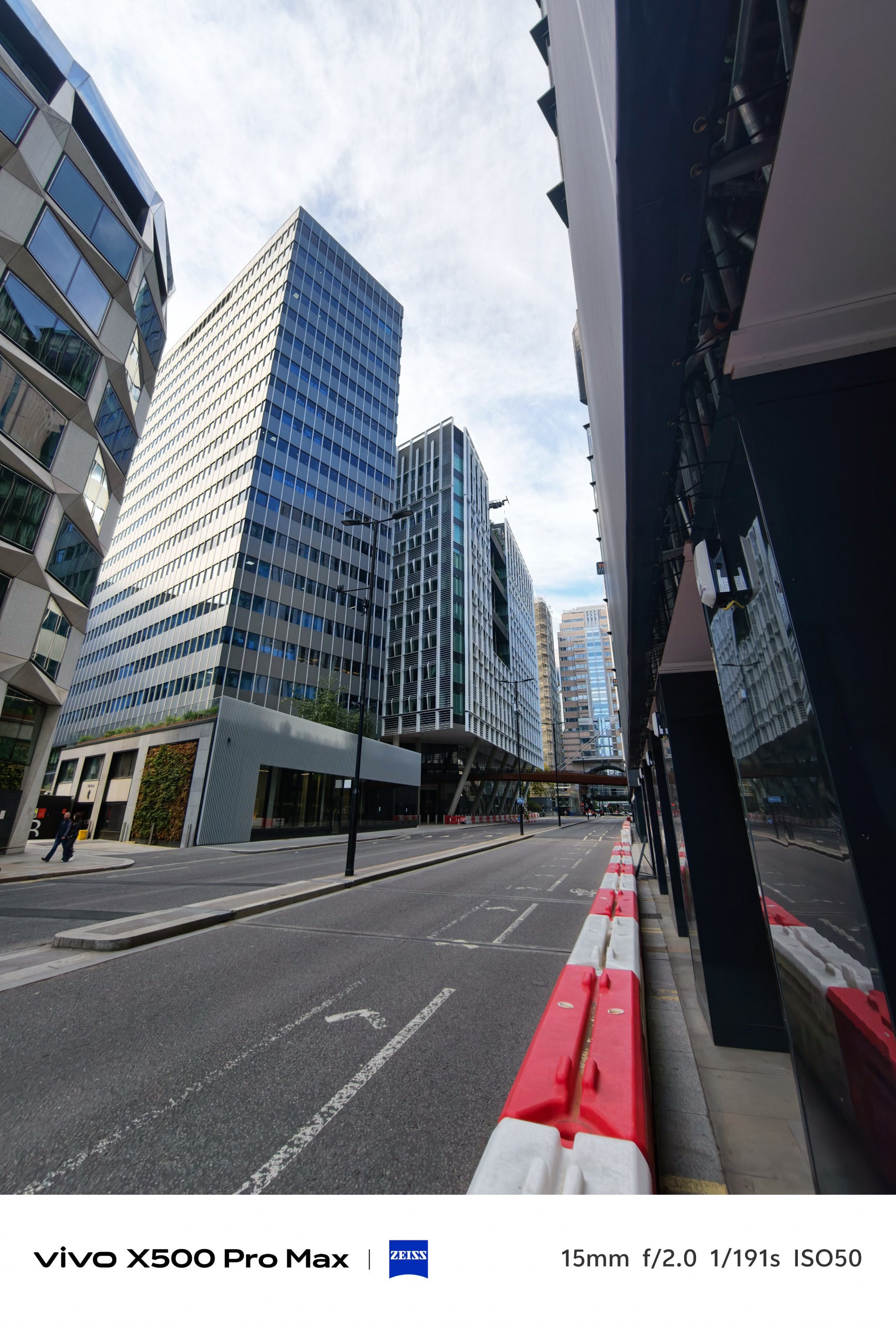 Wide-angle view along a quiet London street lined with modern office towers and red-and-white barriers.